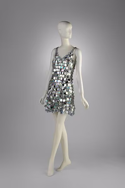 Sleeveless minidress made from rows of iridescent plastic discs joined by metal rings.