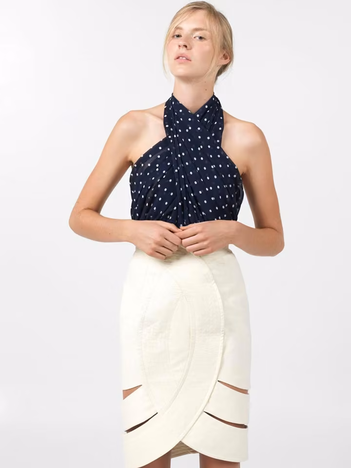 Model in a dark dotted halter top and pale cutout skirt.