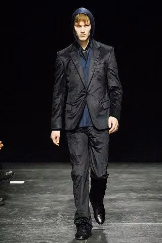 Runway model in a dark suit over layered blue tops.