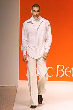 Runway model in a loose white shirt and pale trousers.