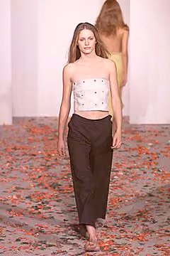 Runway model in a pale embellished strapless top and dark trousers.