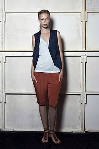 Model in a dark vest, pale blue top and rust-colored shorts.
