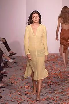 Runway model in a long-sleeved yellow dress with an open neckline.