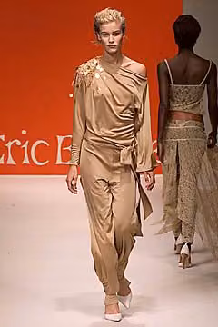 Runway model in a draped bronze one-shoulder top and matching trousers.