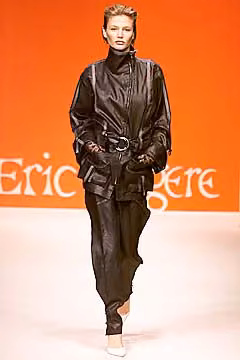 Runway model in a glossy dark jacket and matching trousers.