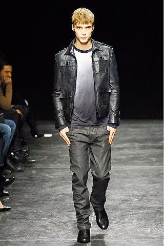 Runway model in a black leather jacket and gray trousers.