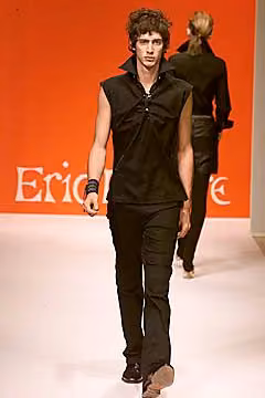 Runway model in a sleeveless black shirt and fitted black trousers.