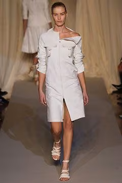 Runway model in an asymmetric white shirtdress with a broad folded collar.