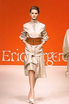 Runway model in a pale belted jacket and layered skirt.