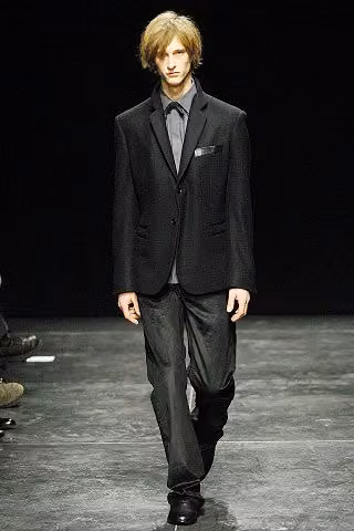 Runway model in a dark suit and gray shirt.