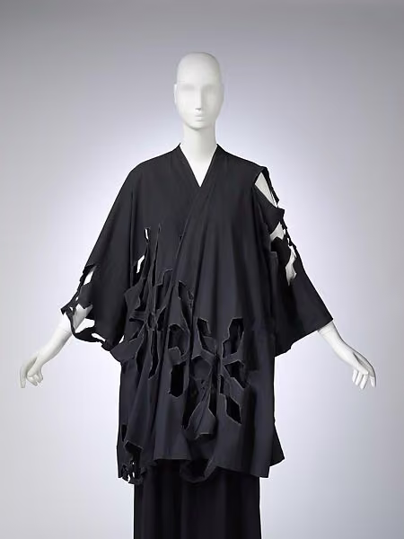 Loose black coat with wide sleeves and large irregular openings through the fabric.
